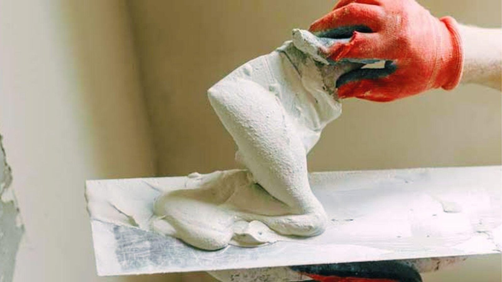 Gloved hand holding thick white plaster mix on hawk ready for smooth interior wall application