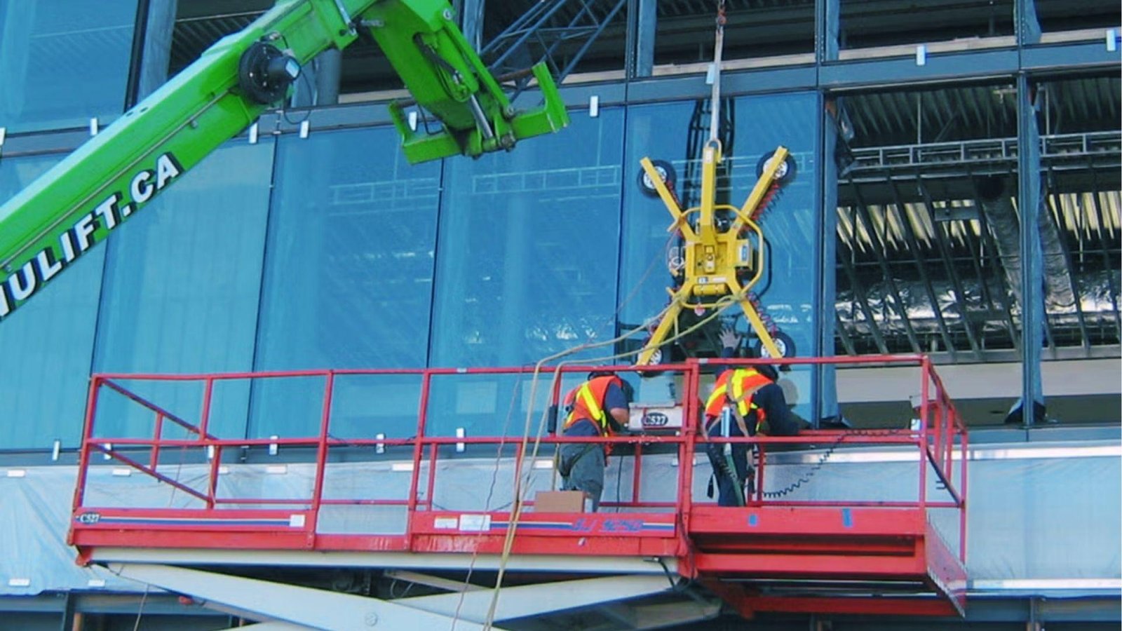 Technicians on scissor lift install glass panels using vacuum lifters for curtain wall testing.