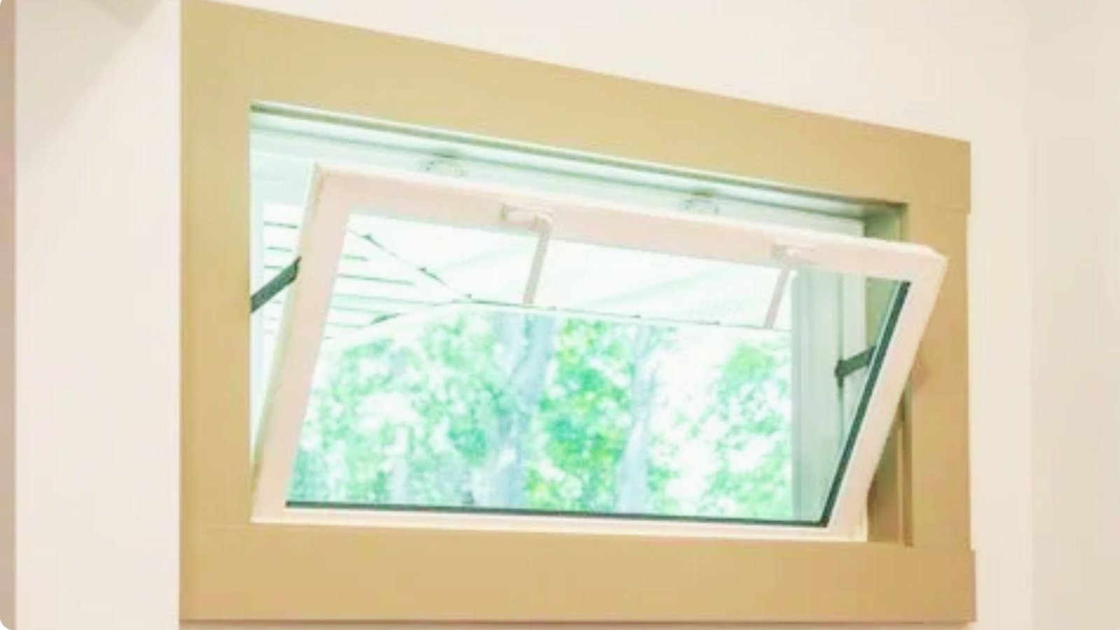 Interior view of white hopper basement window tilted open inward, with wooden frame surround and green trees visible outside.