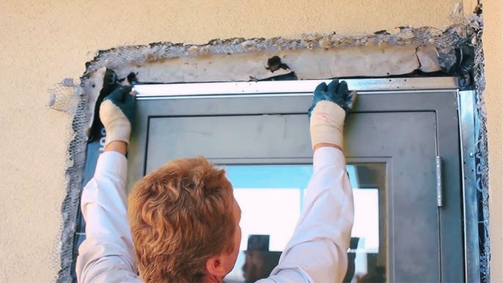 Worker installs metal flashing above door frame on exposed stucco wall for trim prep.