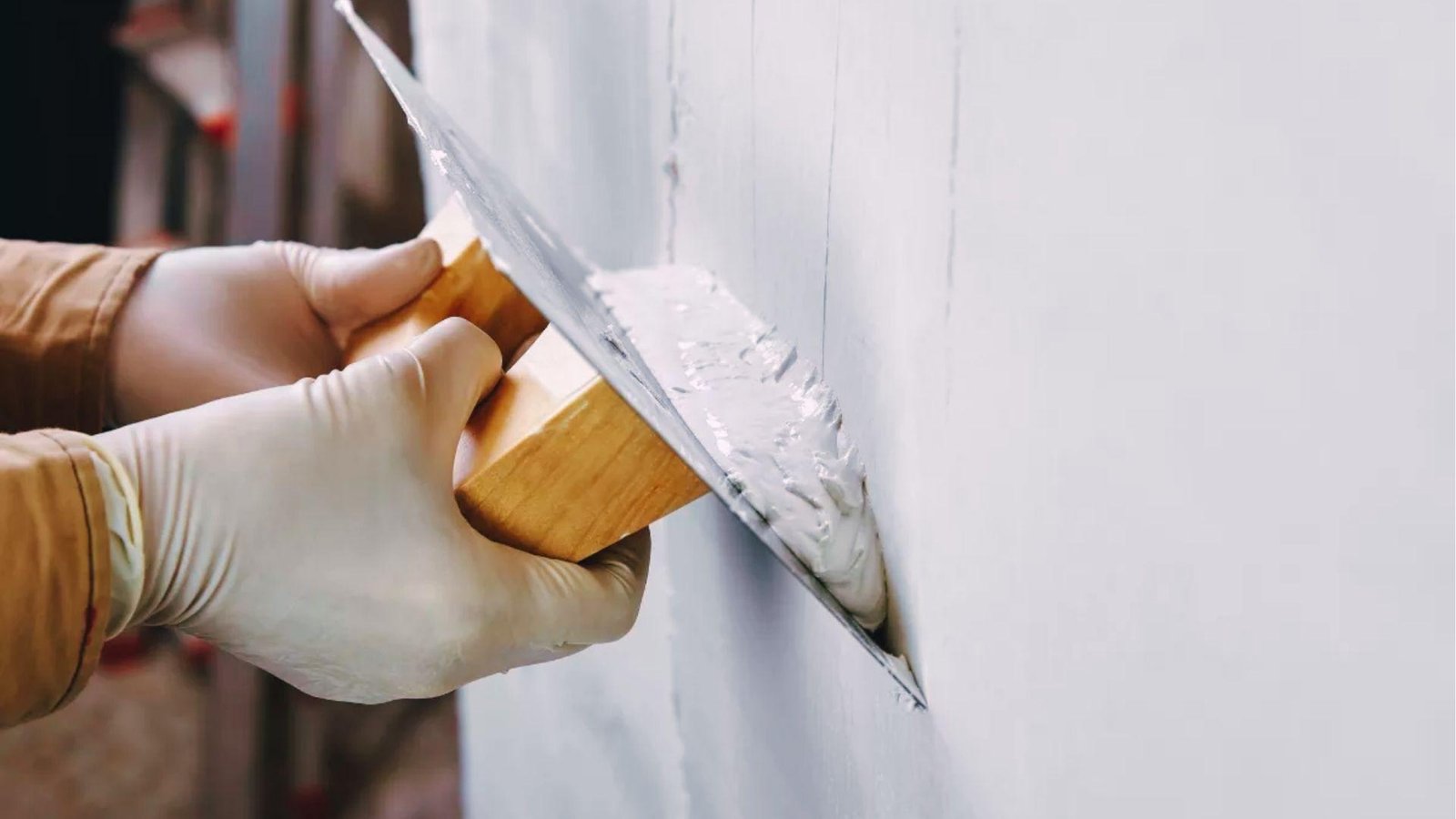 Close-up of hands applying fine white plaster to interior wall for seamless paint-ready surface