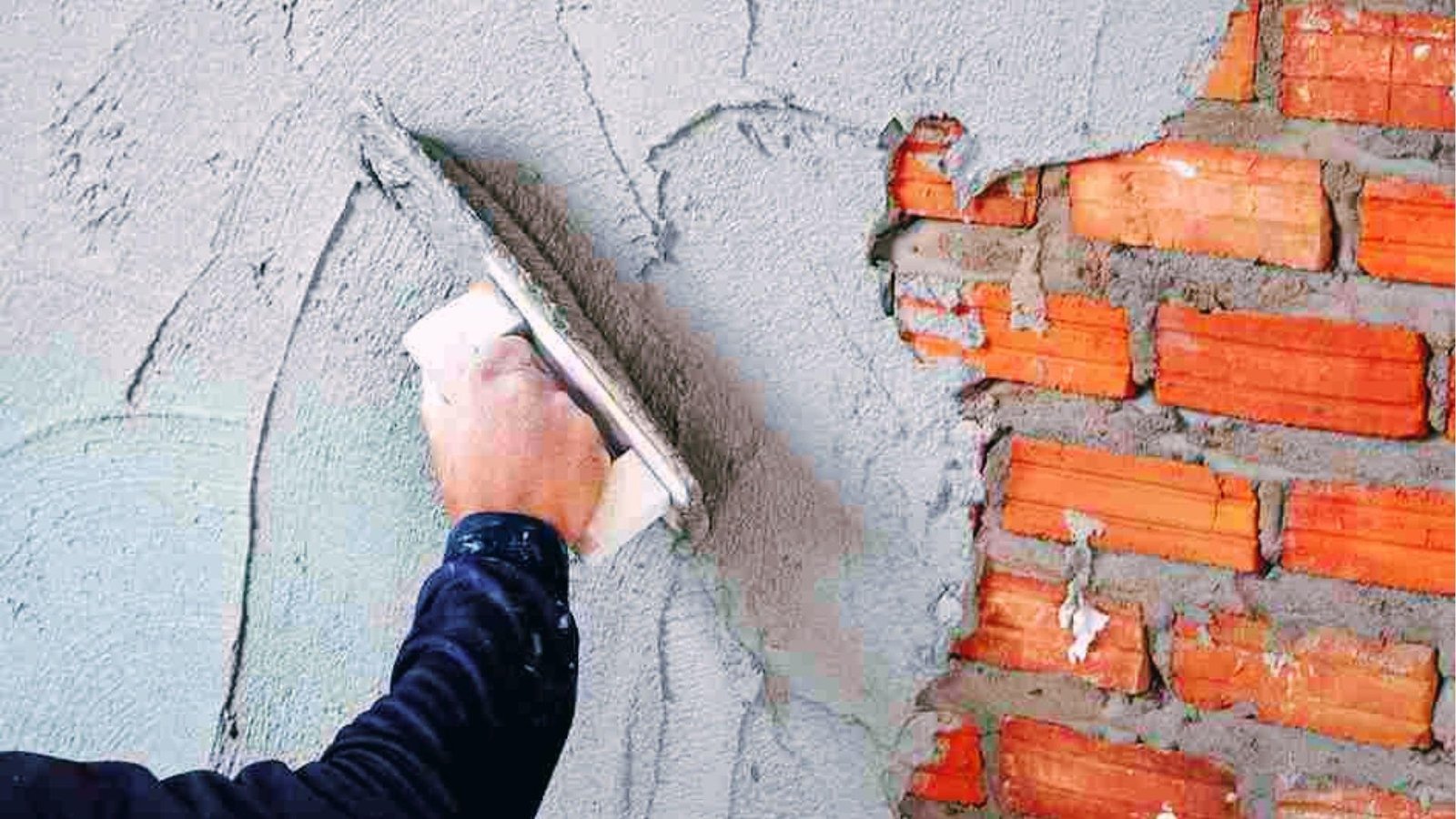 Worker troweling gray cement plaster over exposed red brick wall for strong interior bonding