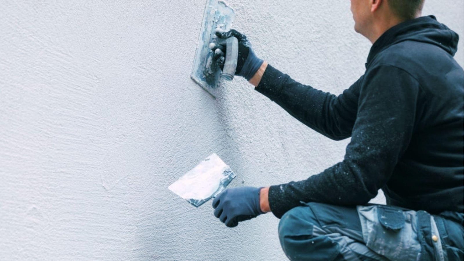 Worker applying textured stucco finish to exterior wall with trowel for durable weather protection
