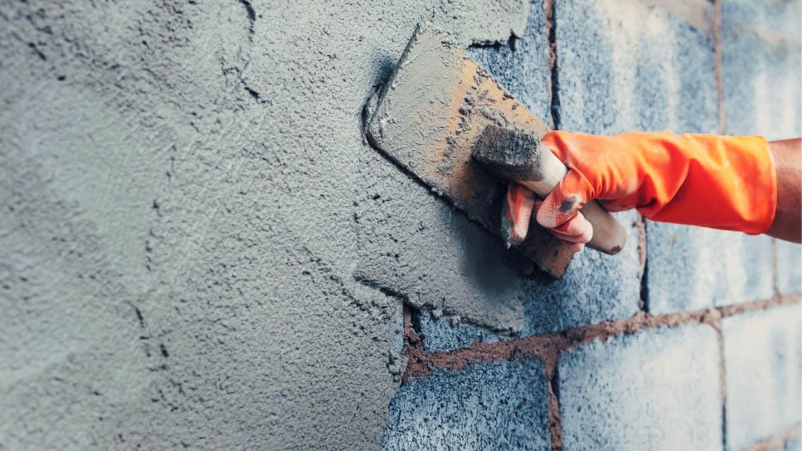 Hand with orange glove spreading coarse stucco render on cinder blocks for exterior durability