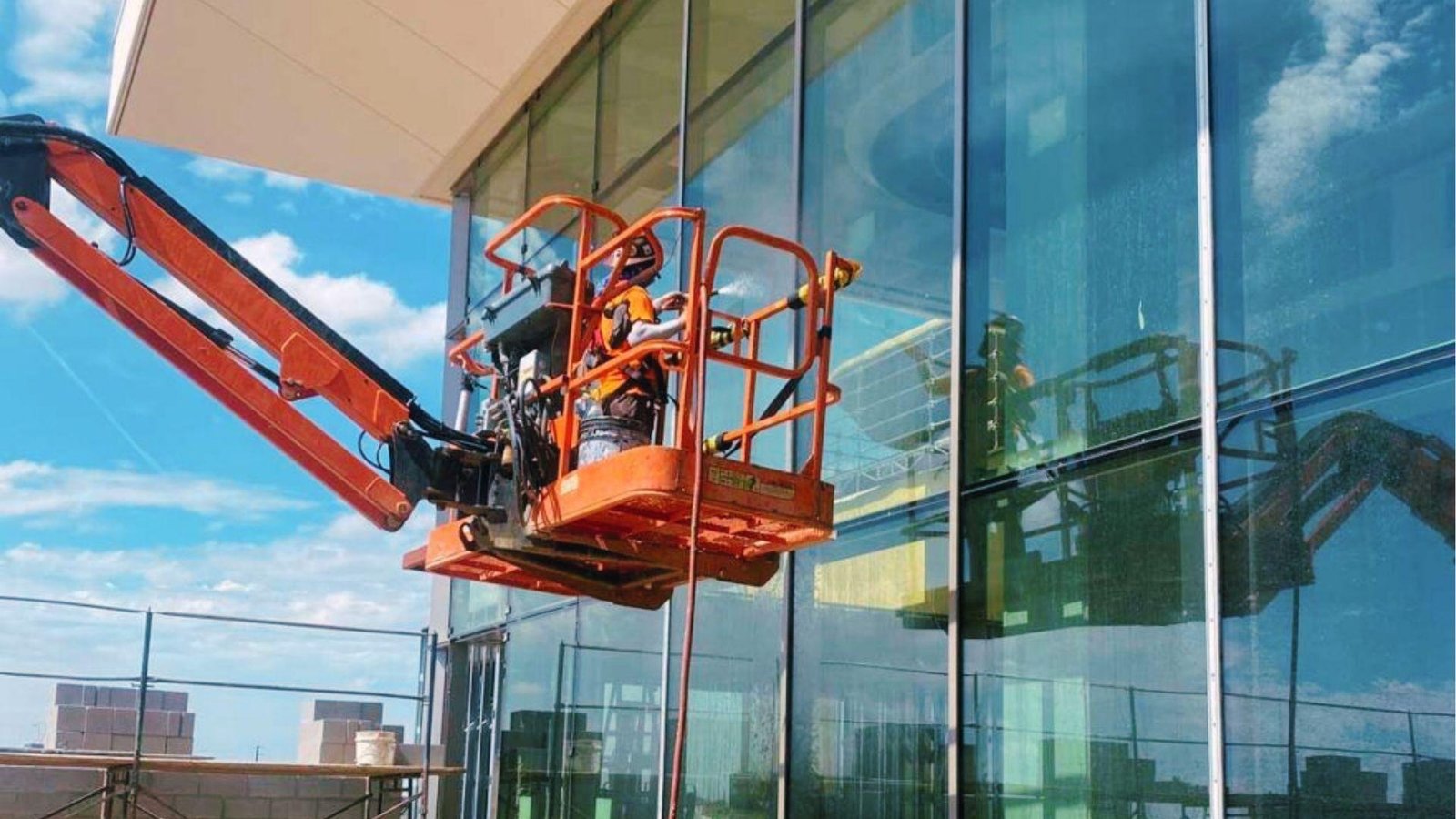 Worker on a boom lift conducts a water spray test on a glass facade for building envelope integrity.
