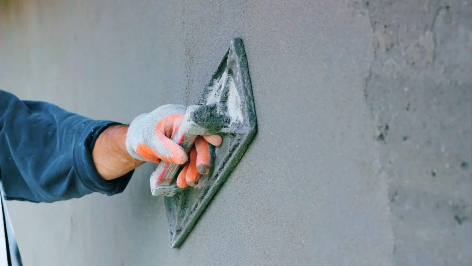 Hand troweling smooth gray stucco base coat on exterior wall showing cement-based exterior mix
